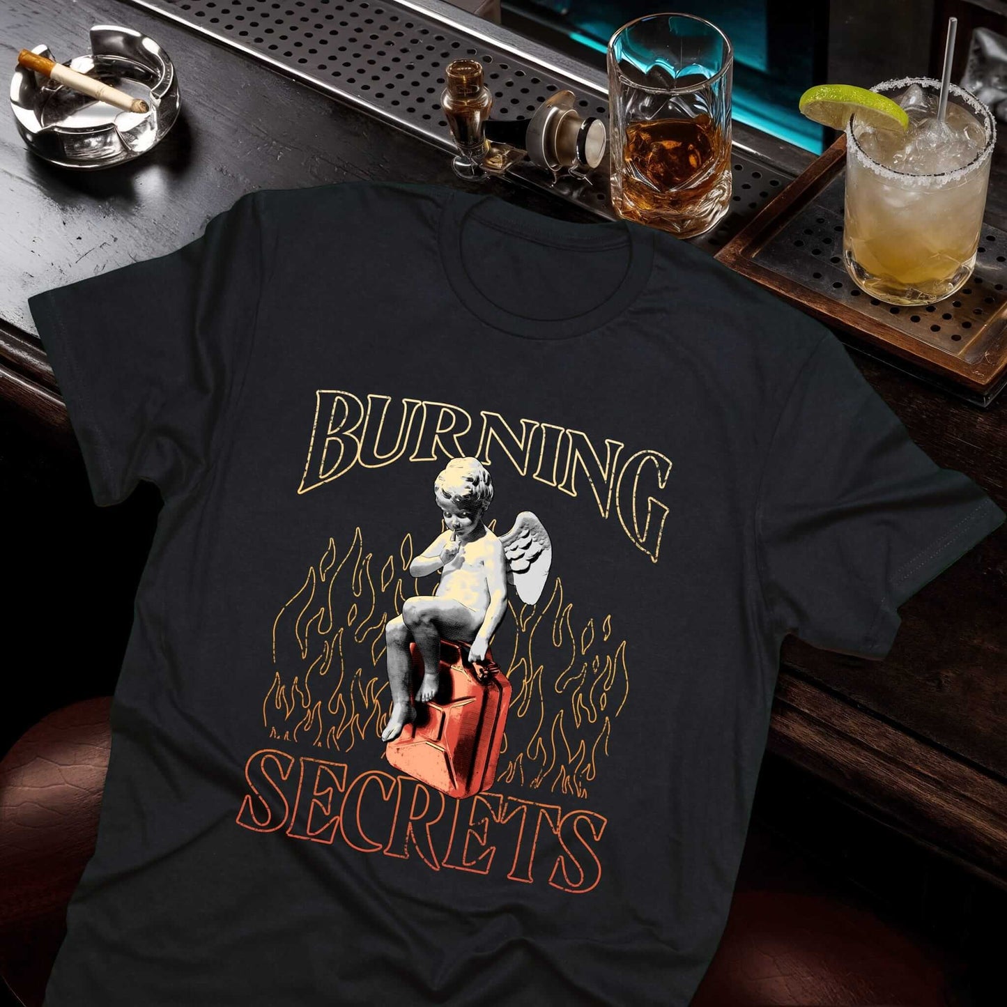 Burning Man black t-shirt with golden yellow text and a cherub angel sitting on a red canister surrounded by flame graphics