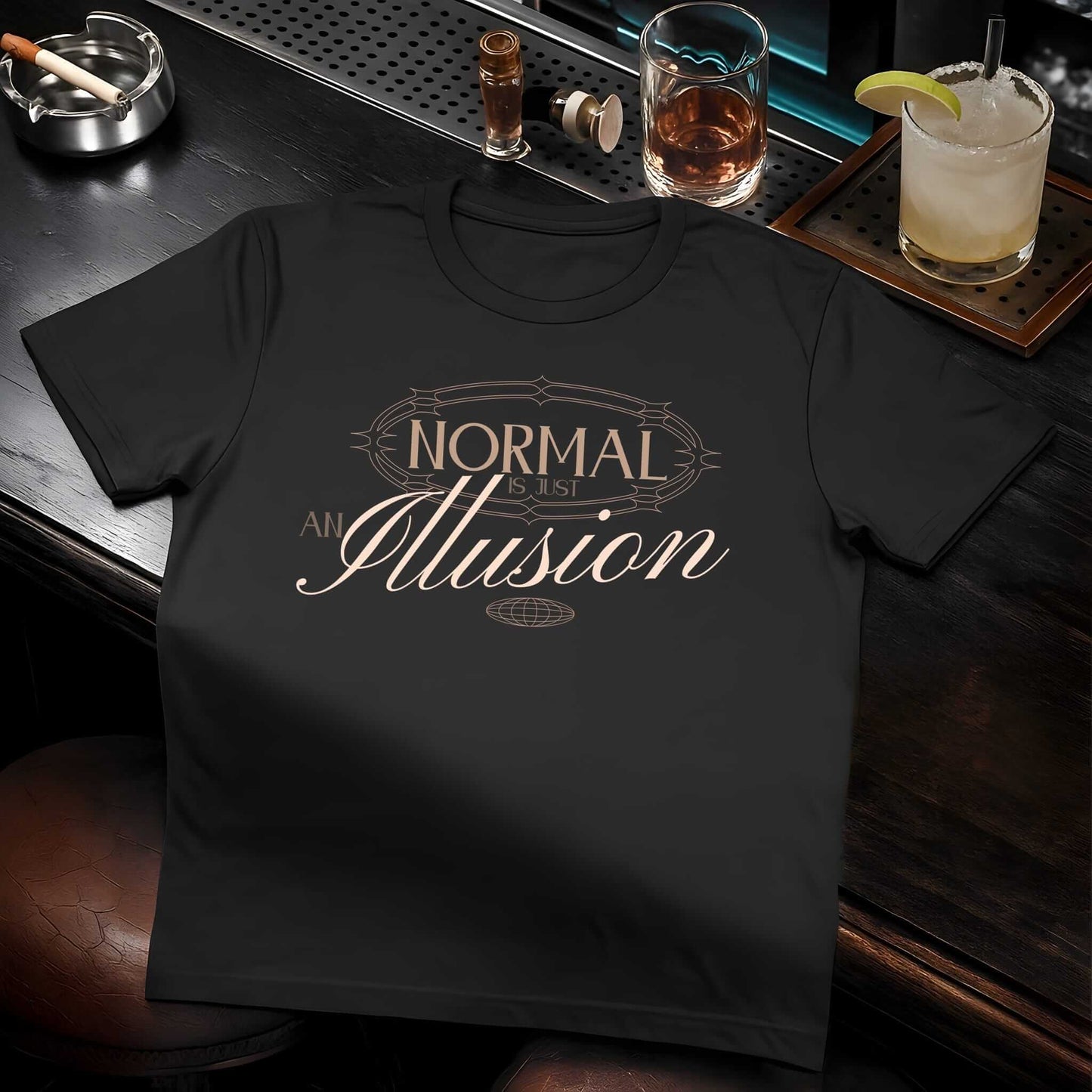 Golden-brown text reading 'NORMAL Is an Illusion' with decorative flourishes in vintage-inspired typography on black t-shirt.