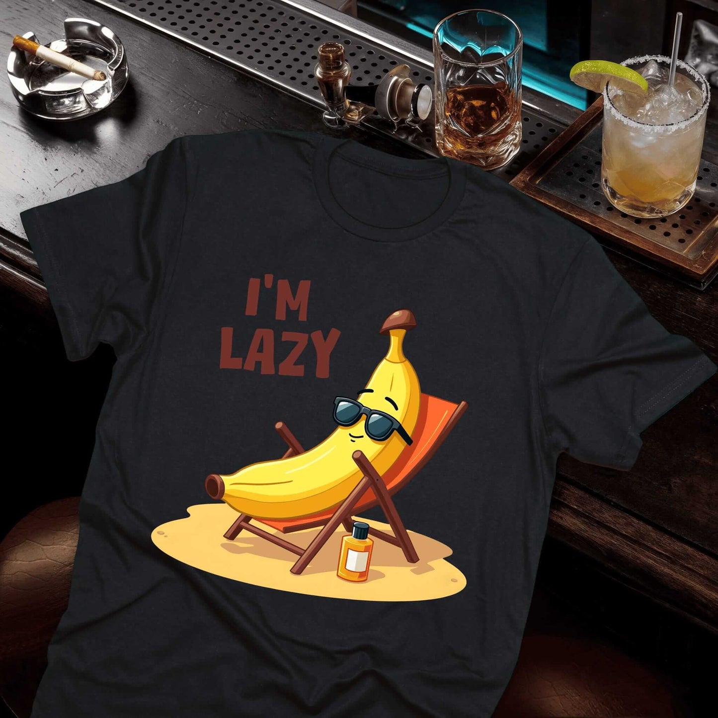 Black shirt featuring a laid-back banana figure with sunglasses sitting in a deck chair, sunscreen nearby on sandy ground