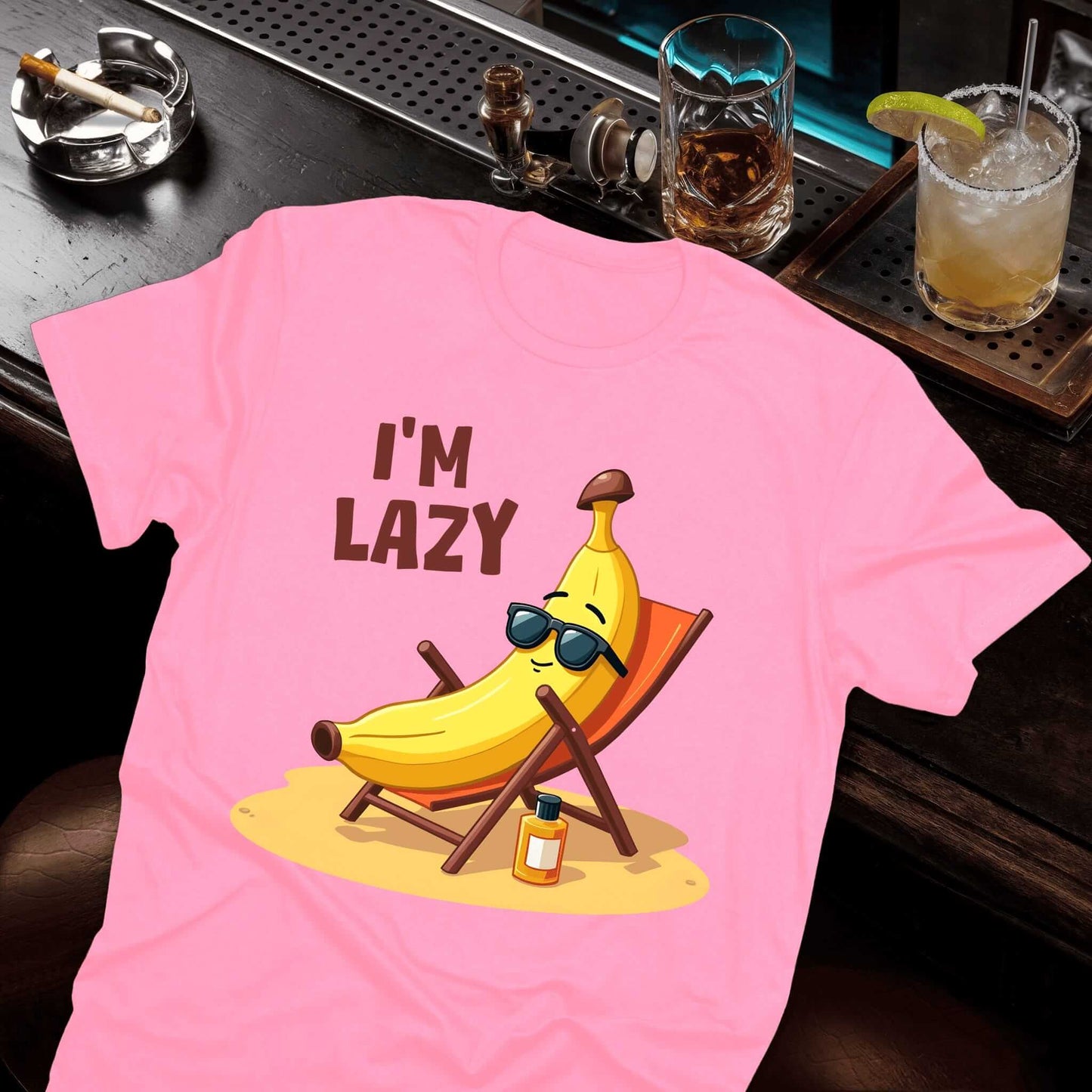 Pink tee with sunglasses-wearing banana lounging casually in a beach chair, sunscreen placed beside the chair