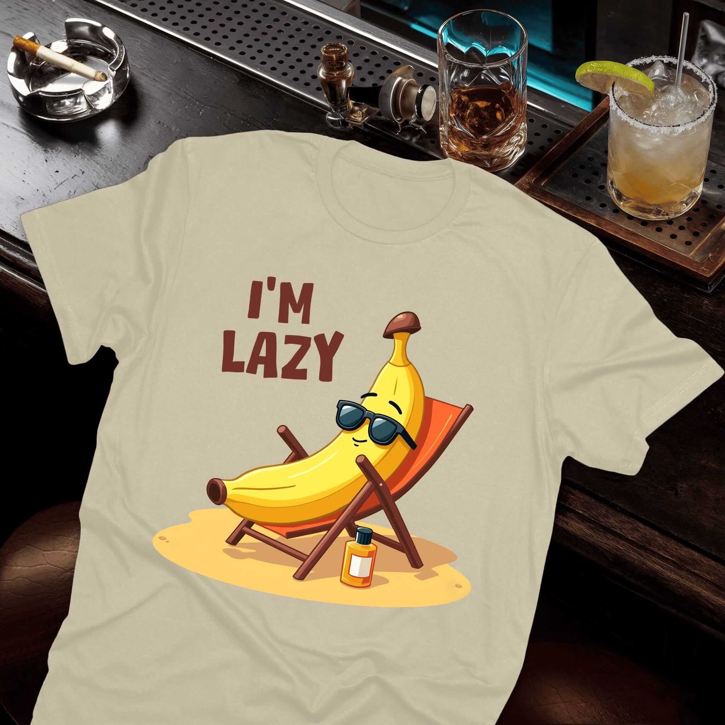 Beige t-shirt featuring sunglasses-wearing banana lounging casually in a beach chair, sunscreen placed beside the chair