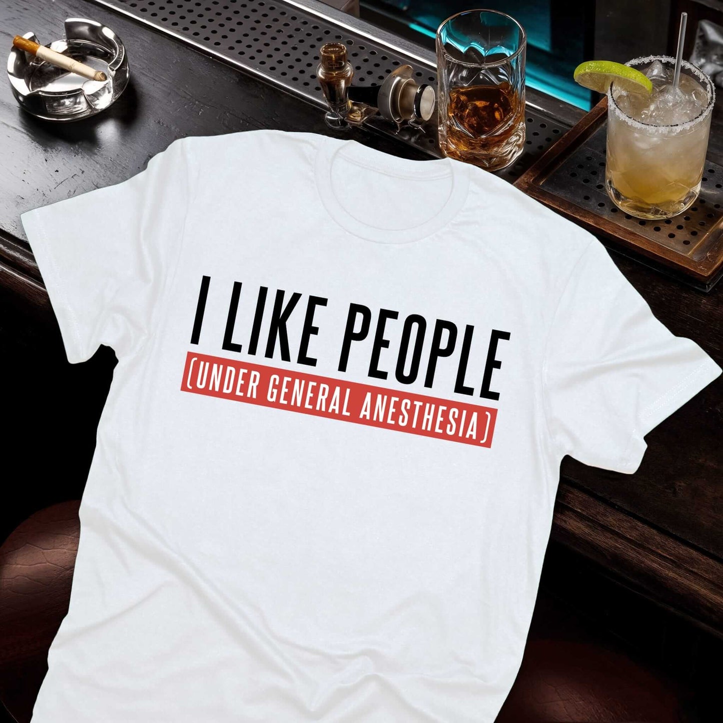Humorous white t-shirt featuring "I LIKE PEOPLE" in bold black letters with red banner reading "UNDER GENERAL ANESTHESIA"