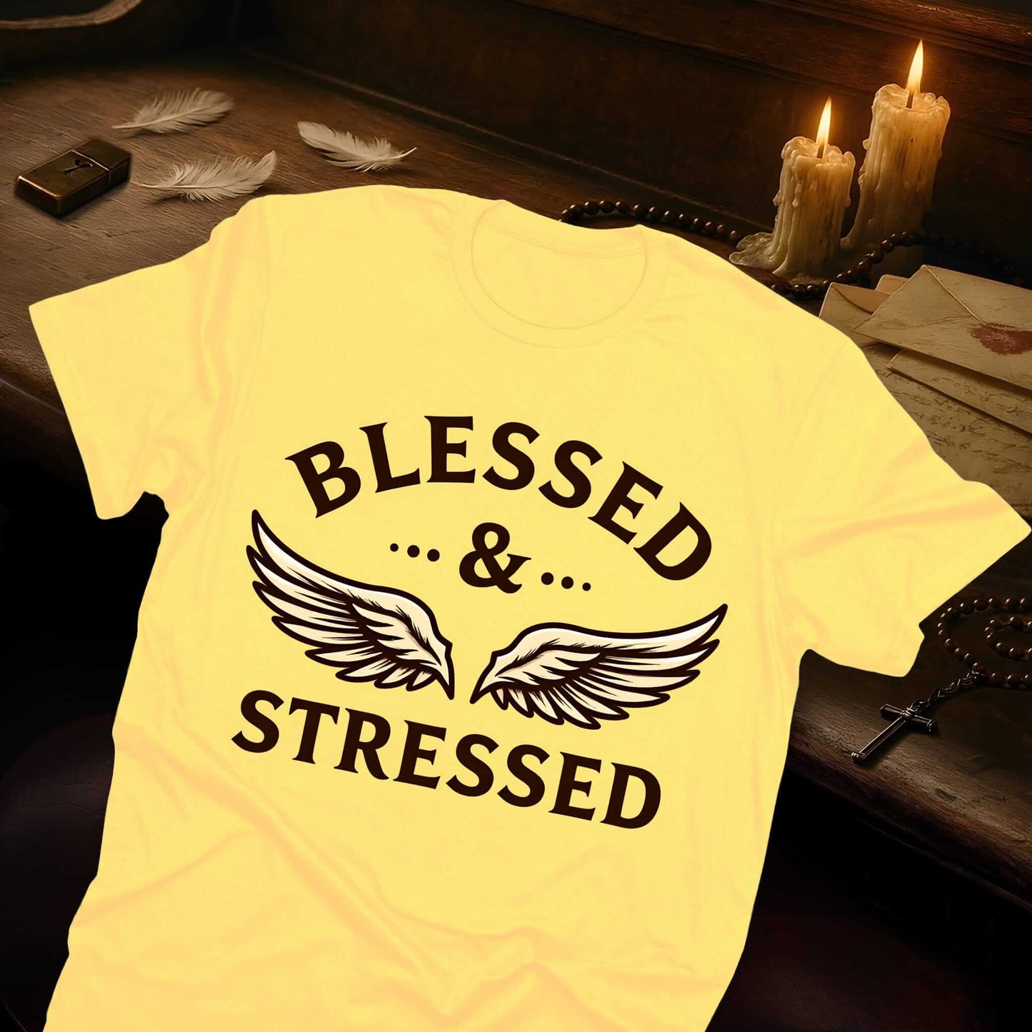 Yellow t-shirt featuring "BLESSED & STRESSED" in bold brown lettering with elegant feathered wings spanning between the word