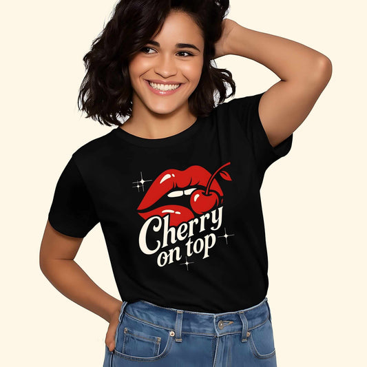 Red glossy lips with bite mark above "Cherry on top" text in white script lettering with sparkle accents on a black t-shirt.