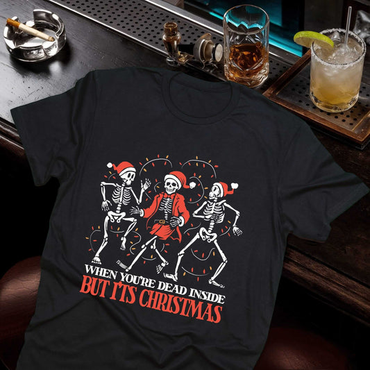 Three dancing skeletons in Santa hats, "When You're Dead Inside But It's Christmas" text on a black t-shirt by Vice and Tees