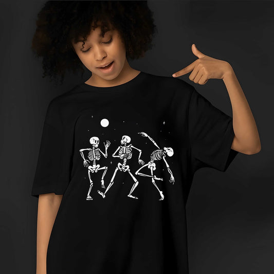 Three white skeleton figures dancing together under a full moon and stars in playful, animated poses on a black t-shirt.
