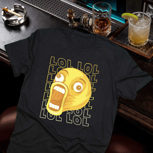 Black t-shirt with yellow laughing meme face and "LOL" text repeated around it, displayed on a bar counter with drinks.