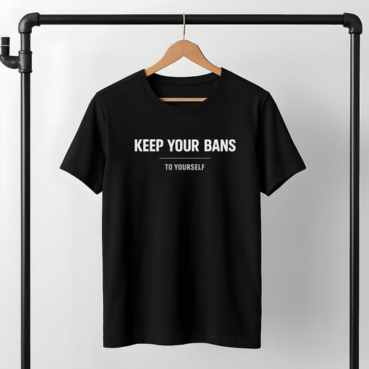 Black t-shirt with white text "KEEP YOUR BANS TO YOURSELF" displayed on wooden hanger against minimalist clothing rack background.