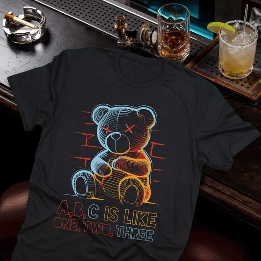 Neon wireframe teddy bear in electric blue and orange with "A,B,C IS LIKE ONE, TWO, THREE" text on black t-shirt