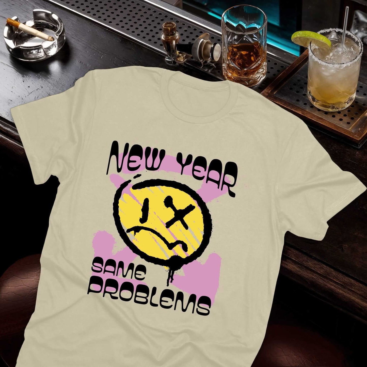 Sarcastic smiley face graphic with crossed-out eye, purple paint splatters, and "New Year Same Problems" lettering on beige.