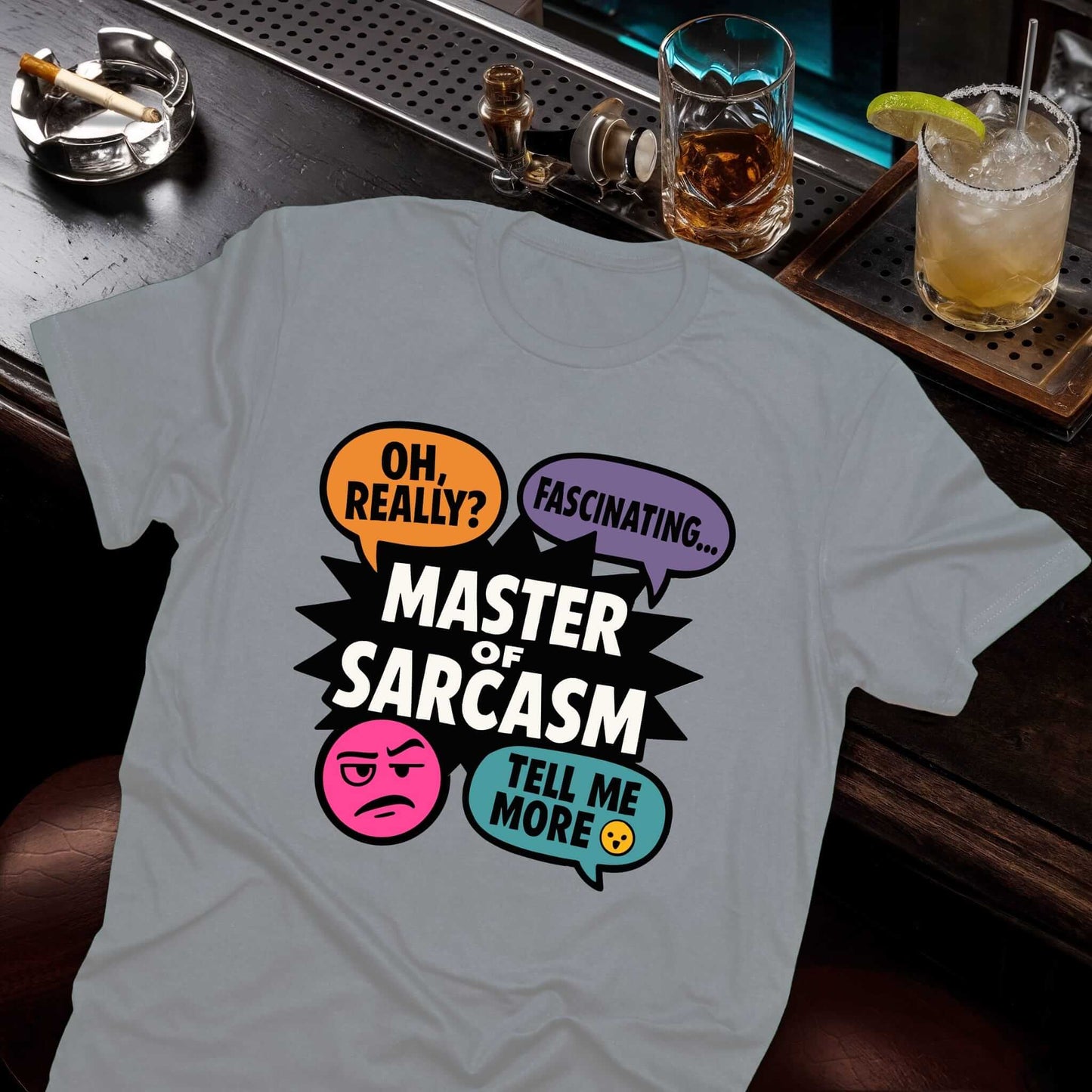 Comic-style sarcasm t-shirt in gray with colorful speech balloons, "Master of Sarcasm" lettering, expressive pink emoji face